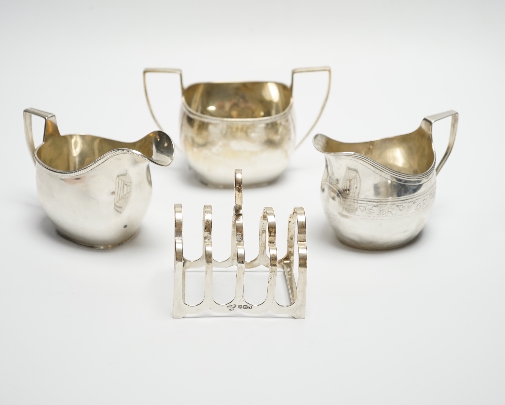 A George III engraved silver cream jug, London, 1808, height 82m, a George V silver cream jug and matching sugar bowl, and a George V silver five bar toast rack, 15.4oz.